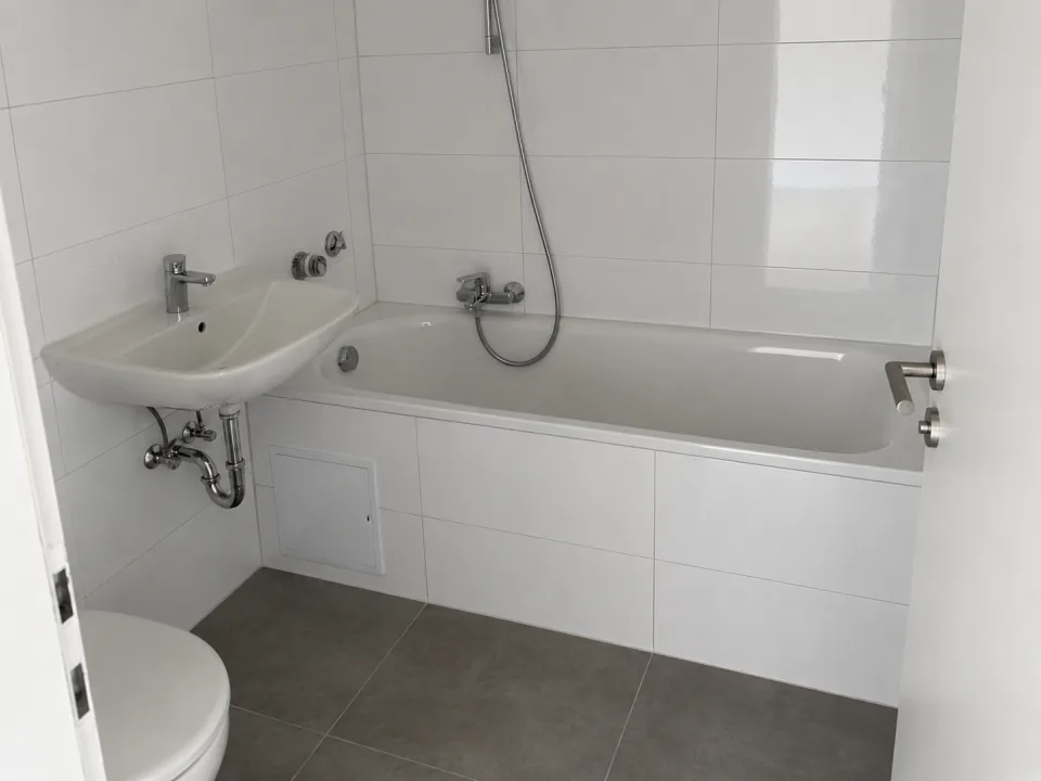 Echtes Referenzfoto eines fertiggestellten Badezimmers mit weißen Fliesen und Badewanne