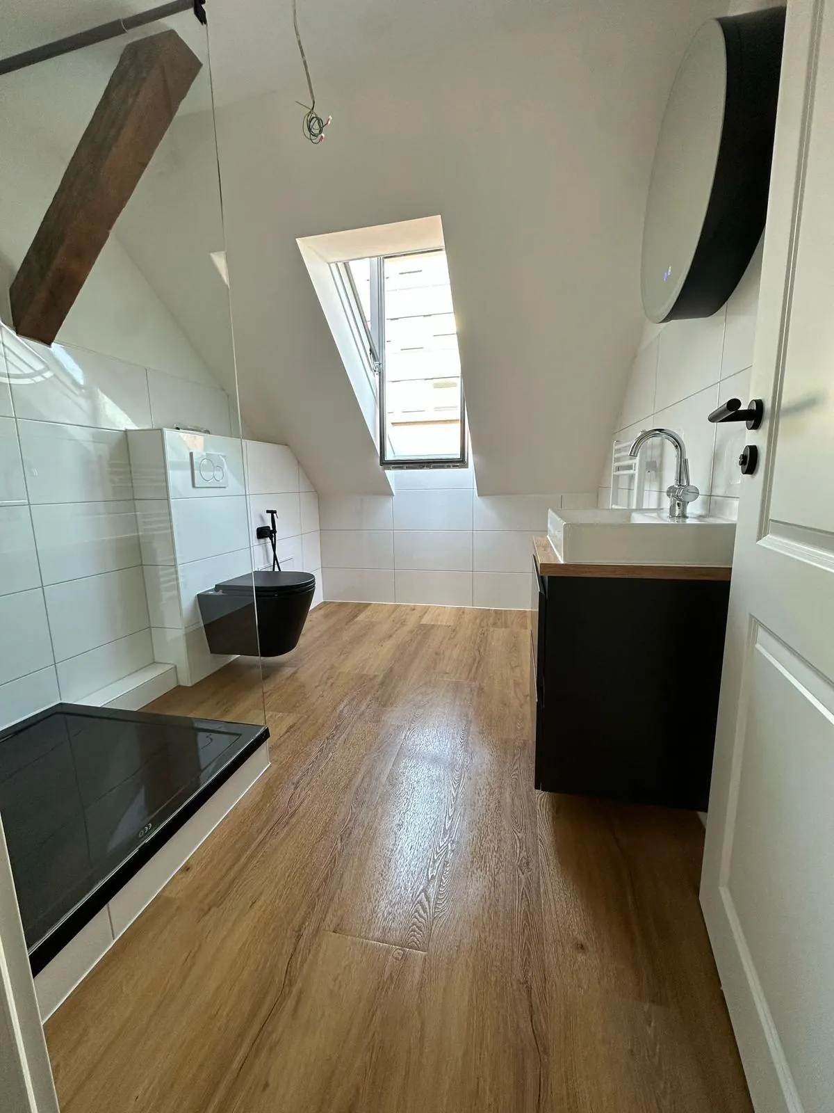 Echtes Referenzfoto eines fertiggestellten Dachgeschossbads mit Glasdusche und Holzoptikboden