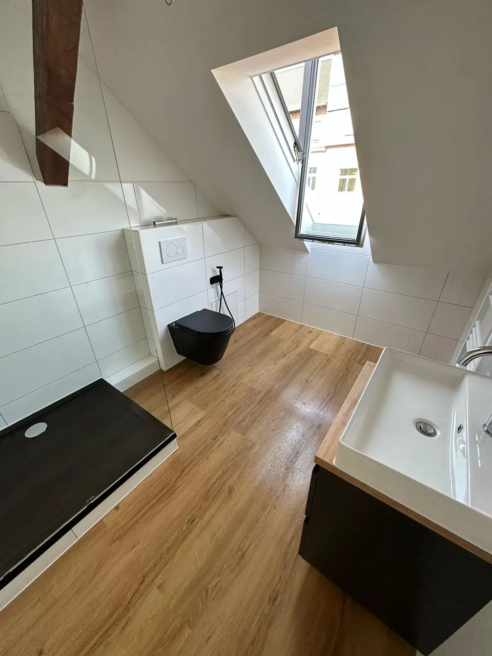Echtes Referenzfoto eines fertiggestellten Dachgeschossbads mit heller Fliese, Glasabtrennung und schwarzem Waschtisch