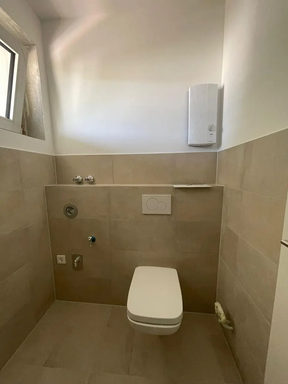 Echtes Referenzfoto eines fertiggestellten Sanitärbereichs mit Wand-WC und beigen Fliesen