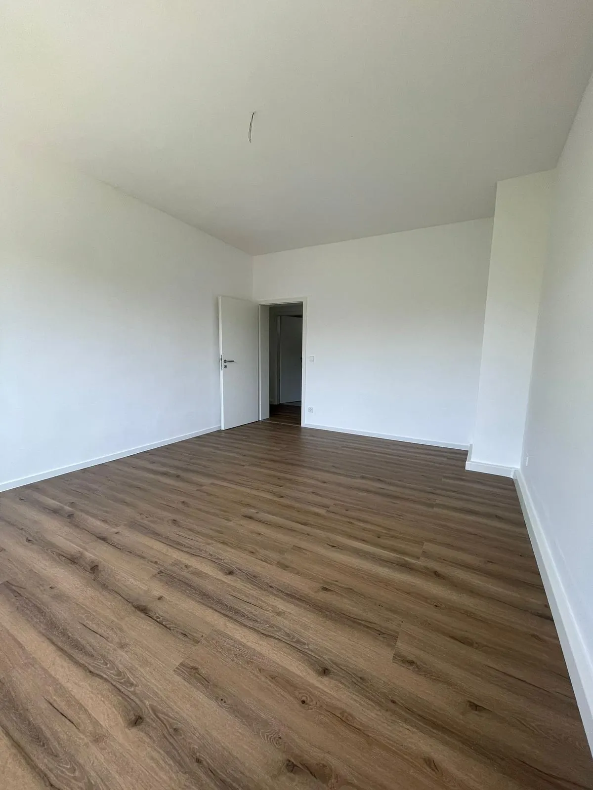Echtes Referenzfoto eines renovierten Wohnraums mit weißen Wänden und Laminatboden