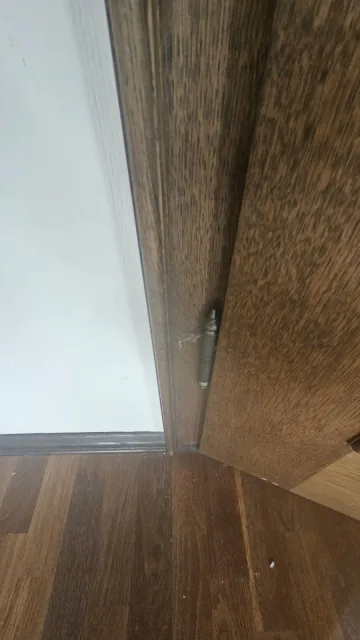 Detail eines dunklen Bodenbelags am Übergang zu einem braunen Türrahmen