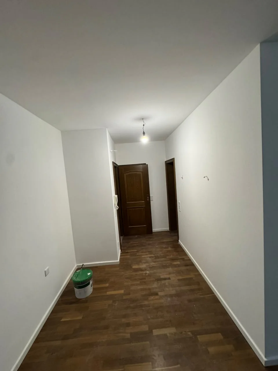 Renovierter Flur mit weißen Wänden, dunklem Boden in Holzoptik und braunen Türen