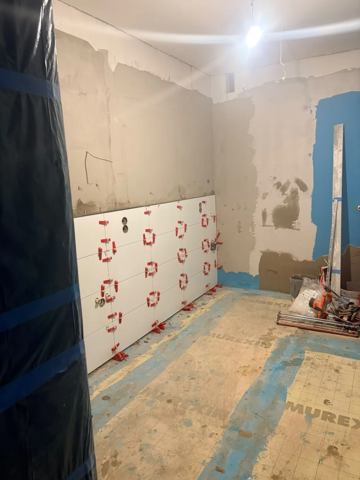 Badezimmer während der Verlegung weißer Wandfliesen mit Werkzeug und offenen oberen Wandzonen