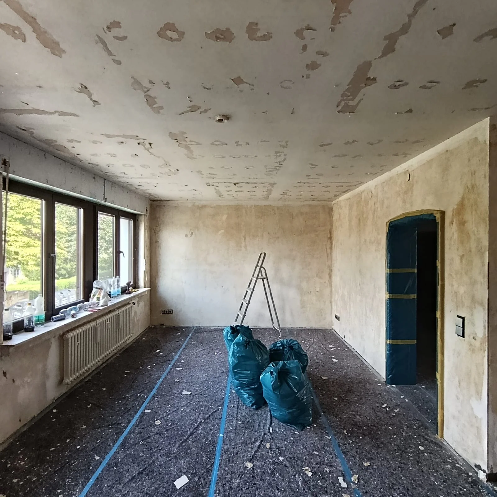 Großer Wohnraum nach der Entkernung mit Fensterfront, offenem Boden und bearbeiteter Decke