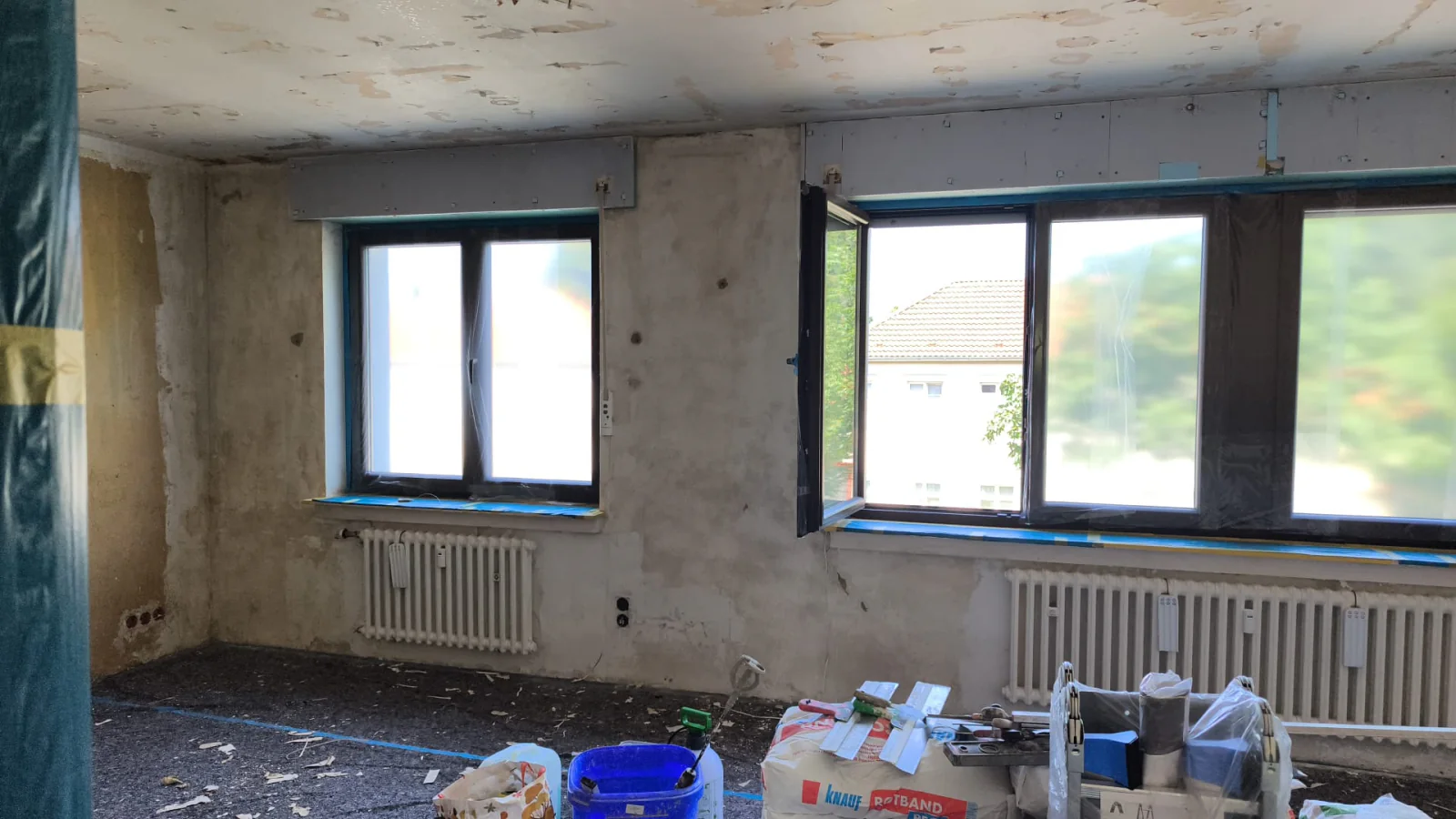 Wohnraum im Ausbau mit vorbereiteten Flächen, Fensterfront, Heizkörpern und Baustellenmaterial